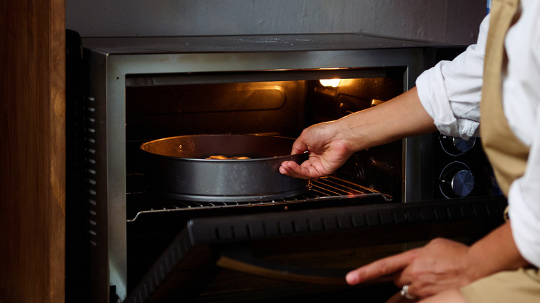 A woman placing a cake pan in an oven