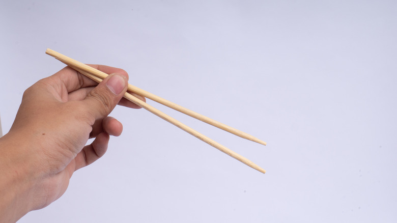 A hand holds a pair of chopsticks
