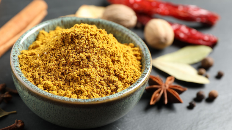 Curry powder in a blue ceramic bowl with a bunch of whole spices on the side