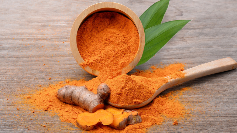 Turmeric powder and root in a wooden bowl and spoon