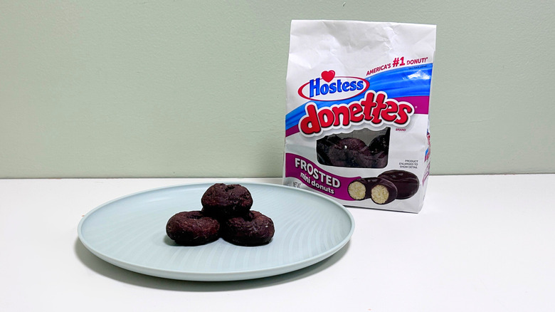 A bag of Hostess Chocolate Donettes next to a green plate of donuts