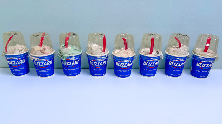 Eight Blizzard flavors in blue cups, with red spoons, lined up in a single row