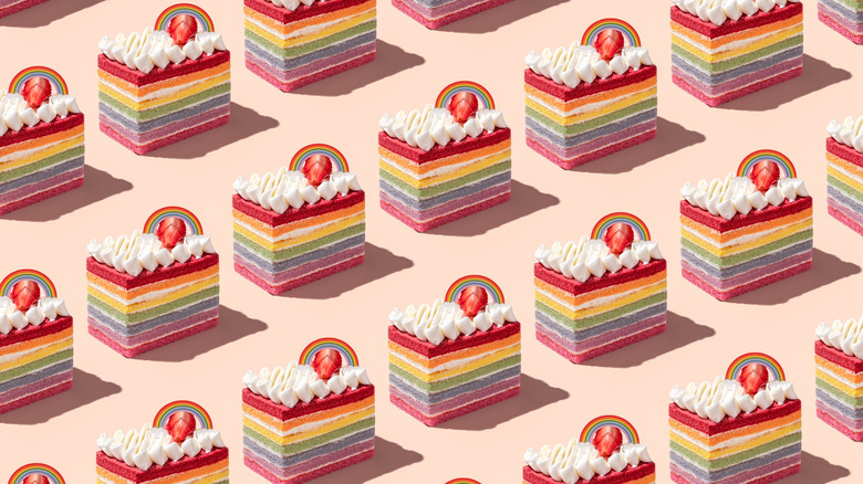 A repeating pattern of whipped cream and strawberry-topped rainbow cakes against a pink background.