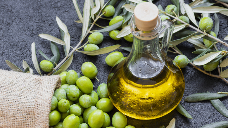 A small bottle of olive oil with green olives and tree branches