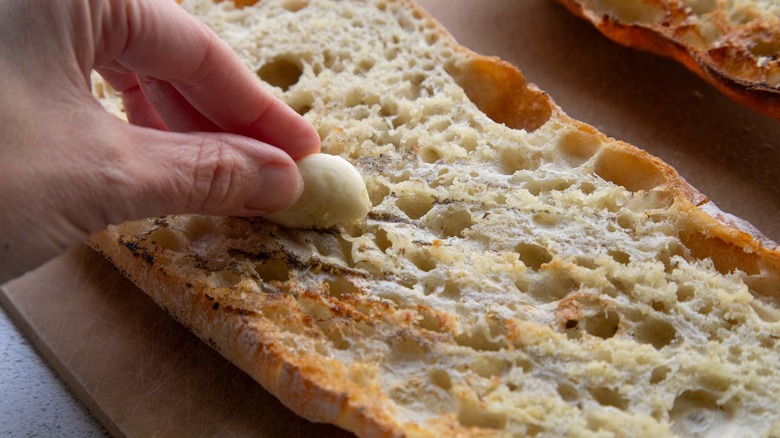 Hand rubbing a garlic clove on a loaf of toasted bread