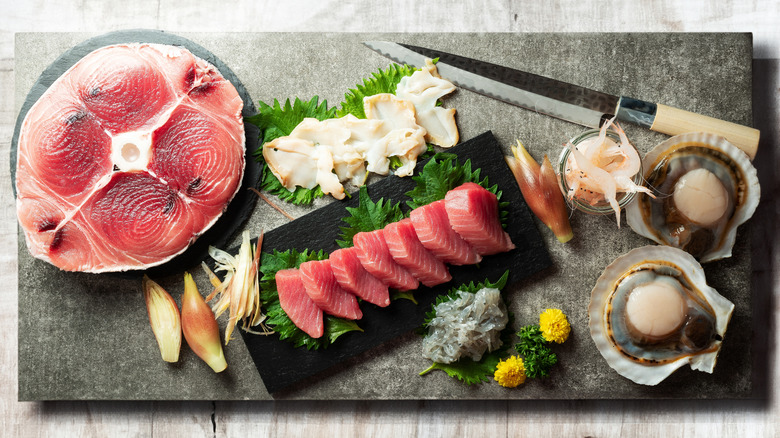 Various raw fish on a slate board with a sushi knife and tuna sashimi