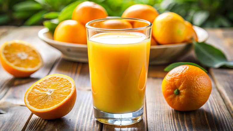 A glass of orange juice surrounded by sliced oranges