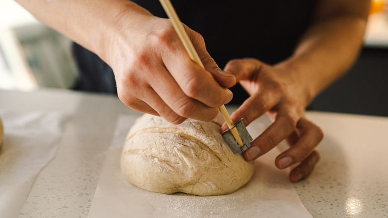 Person scoring surface of a round dough loaf.