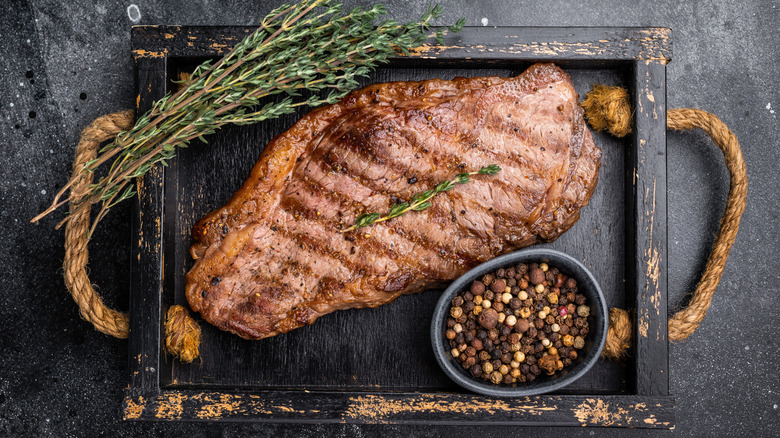 New York strip steak on wooden tray against dark bagrkound